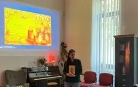 Bibliotekarka stoi przodem do dzieci siedzących na pufach i pokazuje książkę