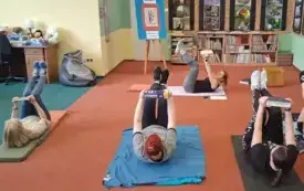 Uczestniczki leżą na podłodze i robią spięcia brzucha, jednocześnie trzymając w wyprostowanych rękach książki w g&oacute;rze. 