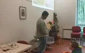 Osoba stoi w miejscu i pokazuje przedmiot - książkę w kształcie zegara.
