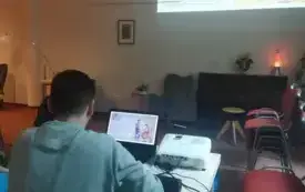 Osoba siedzi przy laptopie i patrzy w ekran, na kt&oacute;rym widoczny jest kolorowy obrazek.