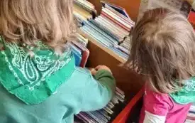 Dzieci przeglądają książeczki w kolorowych skrzyniach.