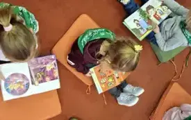Dzieci siedzą na podłodze na kolorowych poduchach i oglądają książeczki.