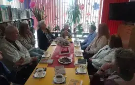 Przy stole siedzie osiem kobiet i mężczyzna, trwa spotkanie DKK. na stole widoczne książki, filiżanki i zakładki.