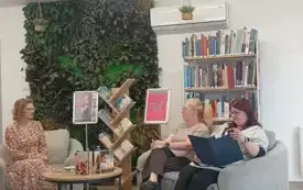 Trzy kobiety siedzą przy stoliku i rozmawiają, w tle regał z książkami