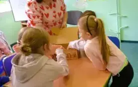 dzieci siegają do kartonowego pudła, kolo nich stoi prowadząca