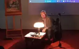 Ryszard Markow siedzi przy stole i przemawia do mikrofonu. Za nim stoi portret Ireneusza Krzysztofa Szmidta