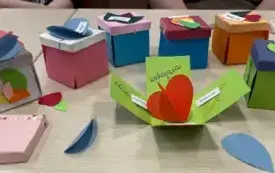 Zbliżenie na zrobione przez dzieci kolorowe pudełka z wypisanymi słowami &bdquo;kochająca&rdquo; oraz &bdquo;cierpliwa&rdquo;.