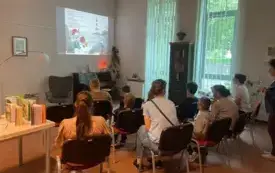 Bibliotekarka stojąca przodem i tłumacząca coś grupie widocznej od tyłu podczas pokazu slajd&oacute;w.