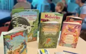 Książki dla dzieci na pierwszym planie oraz dzieci oglądające pokaz slajd&oacute;w w tle.