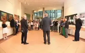 Licznie zgromadzona publiczność słucha przem&oacute;wień organizator&oacute;w podczas wernisażu wystawy fotografii.