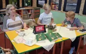 Cztery  Klubowiczki rozmawiają. Przed nimi są filiżanki z kawą. Na stole jest kwiat doniczkowy, tabliczka z logo DKK i cztery omawiane książki