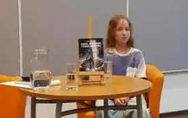 Hanna Krasnowska siedzi przy stoliku, na kt&oacute;rym wyeksponowana jest jej książka