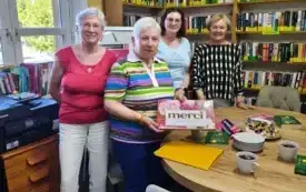 Cztery kobiety stoją przy stole, za nimi regały z książkami