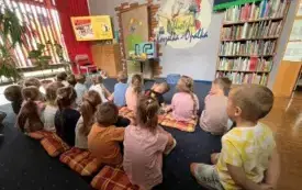 Grupa dzieci siedząca na dywanie ogląda film edykacyjny o pszczołach