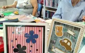 Na stole stoją dwie ramki ozdobione na zajęciach. W jednej z białym obramowaniem są dwa duże kwiaty z pięcioma płatkami wycięte z papieru: jeden czarny, drugi granatowy i 12 malutkich kwiatk&oacute;w w tych dw&oacute;ch kolorach. Kwiaty są na tle w czerwono białe pa