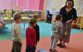Po lewej stronie w rzędzie stoją chłopcy. Bibliotekarka stoi przed nimi. W ręku ma medal z Plastusiem.