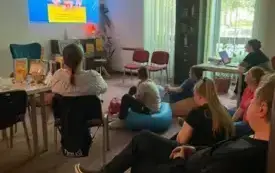 uczestnicy siedzą na kolorowych pufach i oglądają prezentację na ścianie