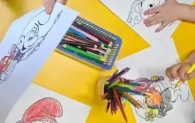 Na środku ż&oacute;łtego stolika znajdują się pojemniki z kredkami. Dzieci kolorują obrazki ze smerfami używając wielu barw. 