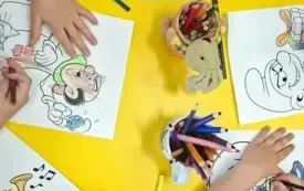 Dzieci przy ż&oacute;łtym stoliku kolorują obrazki ze smerfami i Gargamelem.