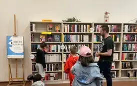 Bibliotekarz stoi przed regałami z książkami i opowiada o zasadach korzystania z biblioteki