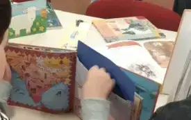 rozłożona książka z kopertą w środku, ręka wyciagająca jej zawartość