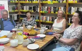 Osoby siedzą przy stoliku, w tle regał na książki.
