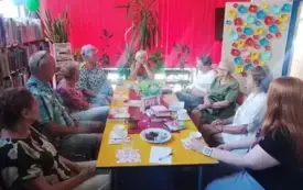 Osiem kobiet i mężczyzna siedzą przy stole, na stole książki kwiaty w wazonie, filiżanki, trwa spotkanie DKK