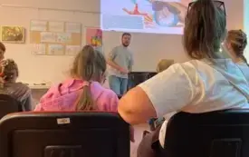Osoby siedzące na krzesłach, w tle prezentacja multimedialna wyświetlana na ścianie.