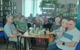 Osoby siedzą przy stole, w tle wnętrze biblioteki.