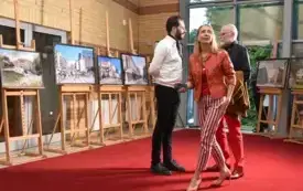 Agata Kaczuk-Jagielnik rozmawia z gośćmi w łączniku Biblioteki Herberta przed fotografiami Piotra Jagielnika prezentowanymi na drewnianych sztalugach w ramach wystawy &bdquo;Miasto w kadrach fotografa i malarki&rdquo;.