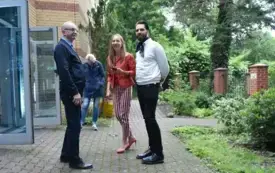 Agata Kaczuk-Jagielnik, wsp&oacute;łautorka wystawy &bdquo;Miasto w kadrach fotografa i malarki&rdquo;, wita gości przed wejściem do łącznika Biblioteki Herberta. W tle widoczny jest ogr&oacute;d przy bibliotece.