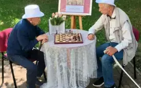 Dw&oacute;ch Pan&oacute;w siedzących przy stoliku, grających w szachy. Panowie ubrani są w stroje z lat ubiegłych.