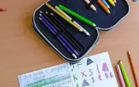 st&oacute;ł, na kt&oacute;rym znajdują się pi&oacute;rniki, zeszyty oraz kredki.