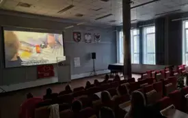 Przyciemniona sala biblioteki Herberta, na ścianie wyświetlany materiał.
