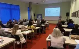 Osoby siedzące w ławkach, w pomieszczeniu panuje jasność.