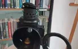 Zabytkowa, metalowa lampa naftowa eksponowana w bibliotece.