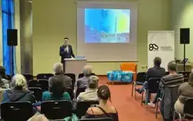 Zdjęcie przedstawia dra Grzegorza Urbanka wygłaszającego referat. Wykonano je dokładnie jak samo jak w przypadku poprzednich prelegent&oacute;w.