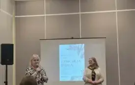 W tle prezentacja na ekranie, przed publicznością zastępca dyrektora biblioteki przemawia, obok niej stoi prowadząca spotkanie