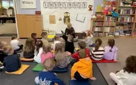 Bibliotekarka czyta dzieciom siedzącym na poduszkach książkę