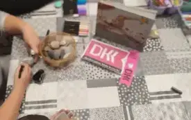 Przy stole dzieci maluja kamienie. Na stole książka i logo DKK