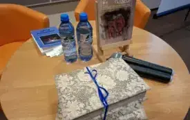 Stolik, na kt&oacute;rym znajduje się numer Pegaza, wody, tomik poezji i przewiązane sznurkiem szkatułki