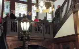 Seniorzy zwiedzają Willę Hansa Lehmanna z przewodnikiem. Wchodzą po schodach i oglądają witraże w oknach.