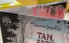 Na stole stoi opakowanie audiobooka, w tle siedzi młodzież.