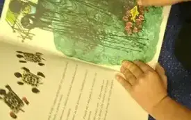 Na dywanie dziecko ogląda ilustrację w książce.