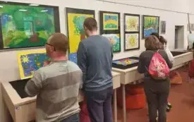 trzy osoby siedzą na środku sali, w tle kolorowa wystawa.