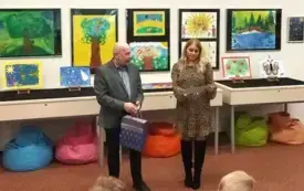 dwie osoby siedzą na środku sali, w tle kolorowa wystawa.