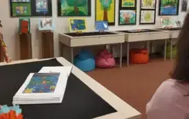 wnętrze biblioteki: wystawa z zawieszonymi na ścianie pracami oraz gablota z kroniką.