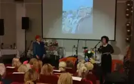 Barbara Schroeder oraz Hanna Kaup przemawiają na scenie, stojąc przed publicznością. W tle prezentowane są zdjęcia przedstawiające działalność Klubu &bdquo;Na Zapiecku&rdquo;.