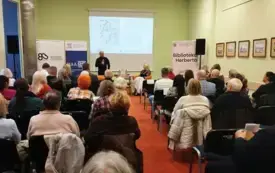 Jakub Niebieszczański przemawia do uczestnik&oacute;w spotkania autorskiego, obok niego przy stoliku siedzi Beata Kukiel-Vraila.