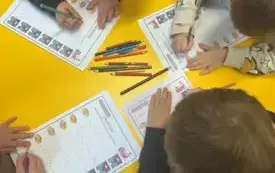 Dzieci przy stoliku wypełniają karty pracy.